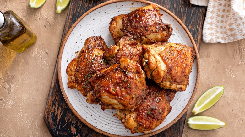 ceramic plate topped with roasted chicken thighs next to a couple of sliced limes