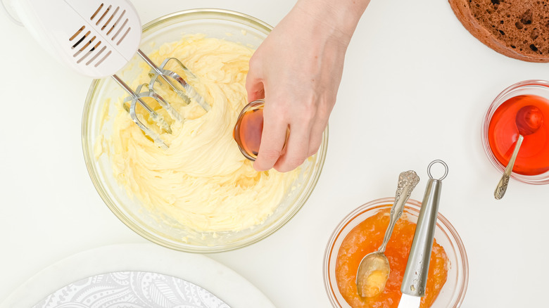 hand pouring liquid into cake batter in bowl while mixing