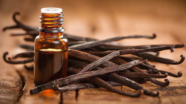 mini bottle of vanilla extract next to whole vanilla beans on a wooden surface