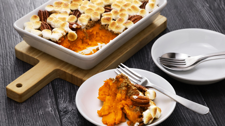 Sweet potato casserole on a wooden cutting board next to plates