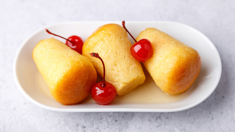 Three baba au rhum cakes soaked in syrup served on a platter with cherries