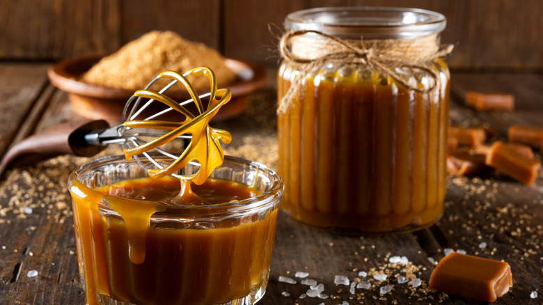 Two glass jars filled with caramel sauce with whisk