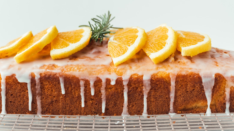 cake with powdered sugar glaze topped with slices of oranges and a sprig of rosemary