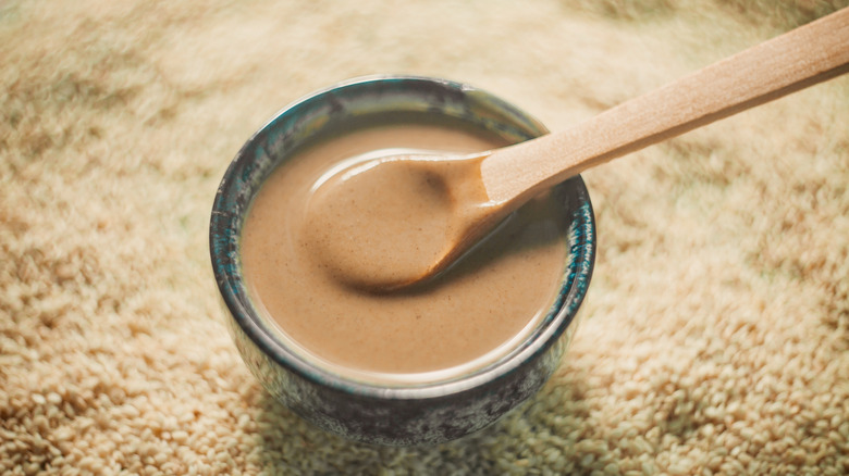 Bowl of tahini in black bowl with wooden spoon