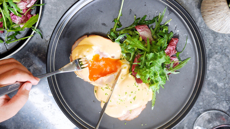 Person cutting open runny poached egg on black plate