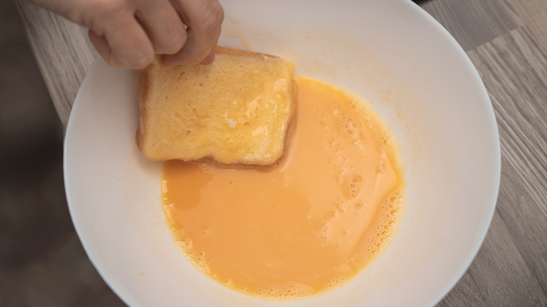 Hand dipping french toast in egg batter