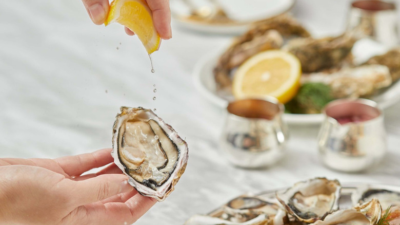 hands squeezing lemon onto half shell oyster