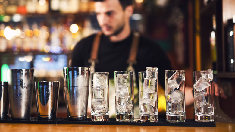 Bartender with row of ice-filled glasses