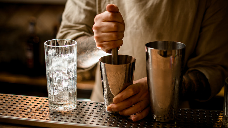 Bartender muddling ingredients in a metal tin