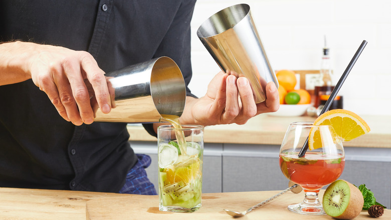 Person mixing drinks with various fruits