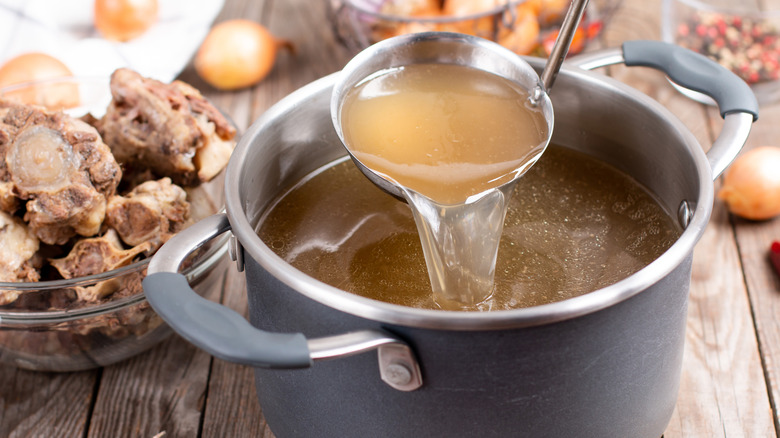 A person ladling bone broth out of a pot