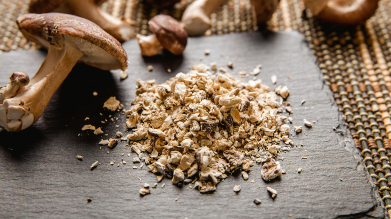 A cutting board with dried shiitake mushroom powder next to whole shiitake mushrooms