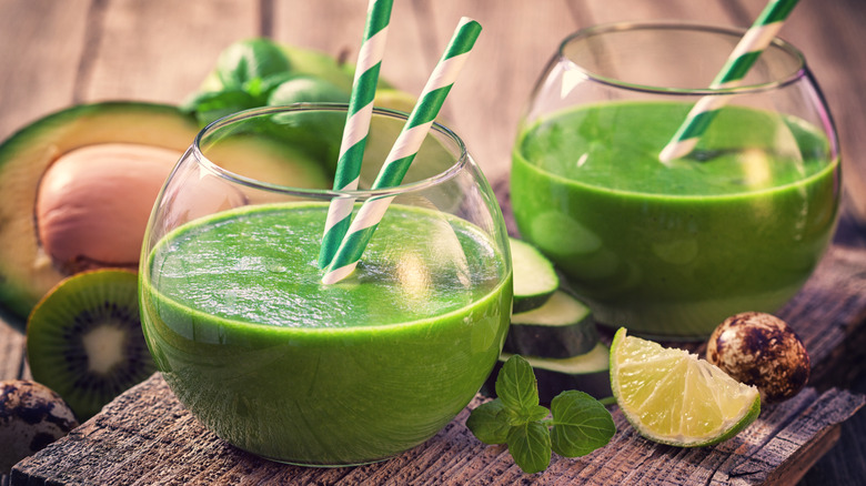 Two avocado margaritas on a cutting board with avocado and limes