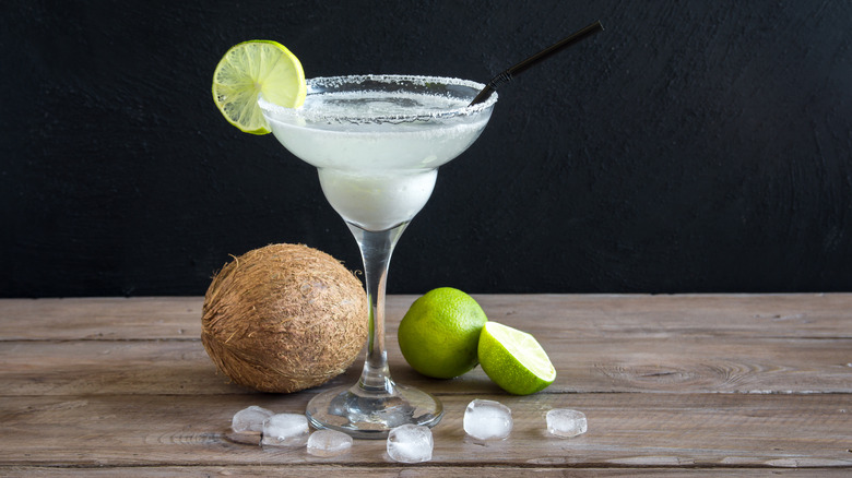 A coconut margarita on a table with a coconut and limes