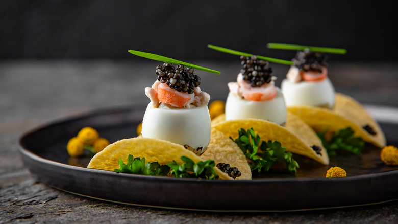A plate of potato chips topped with quail eggs, shrimp, caviar, and chives