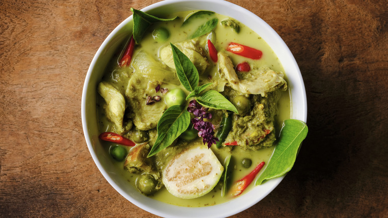 A white bowl of Thai green curry on a wooden table