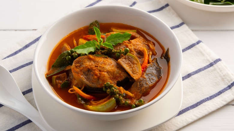 A white bowl of jungle curry with herb garnish