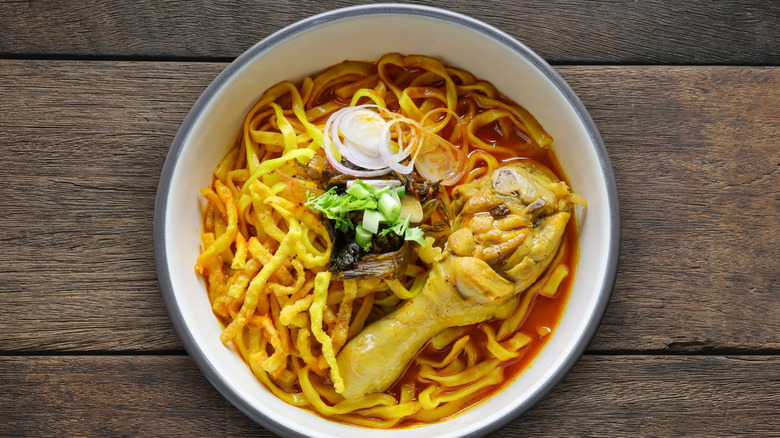 A white bowl of khao soi on a wooden table