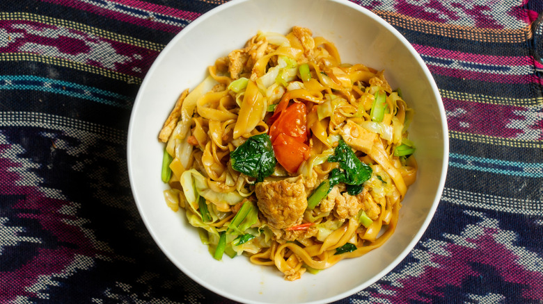 A white bowl with drunken noodles on a patterned blanket