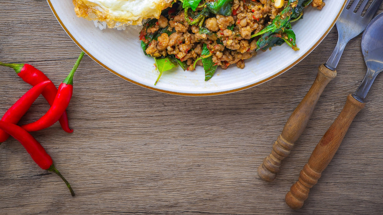 A white plate with Thai basil minced pork, rice, and a fried egg