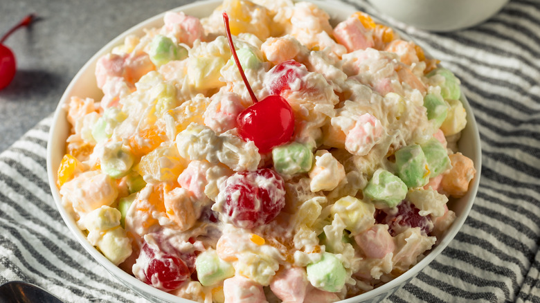 A white bowl of ambrosia salad topped with a maraschino cherry