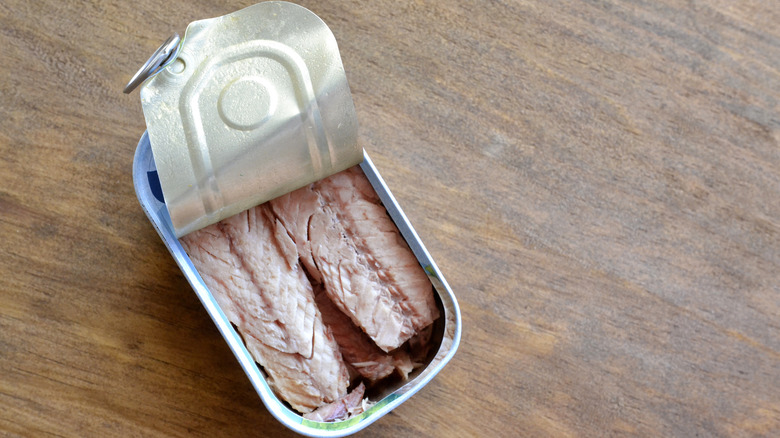 A tin of anchovy with the lid peeled back on a wooden table