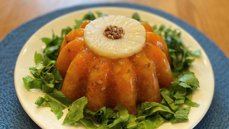 A molded Jello salad with a pineapple ring on top sitting on a bed of lettuce