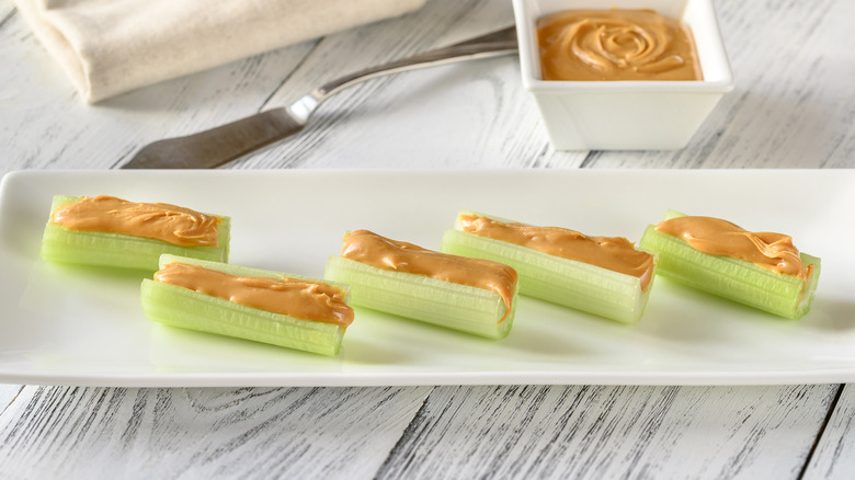 A white tray with celery and peanut butter on a white wooden table