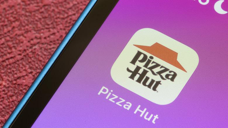 Icon of PIzza Hut's app on a phone with a pink background