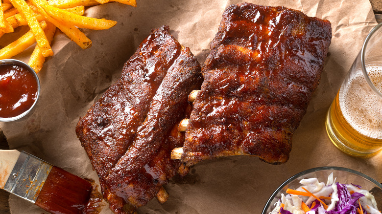 A rack of baby back ribs with french fries, barbecue sauce, and a glass of beer