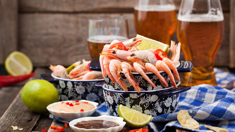 A bowl of cooked shrimp on a table with beer glasses