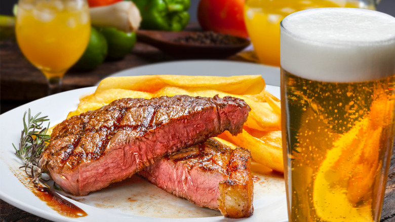 Steak and fries on a plate next to a glass of beer