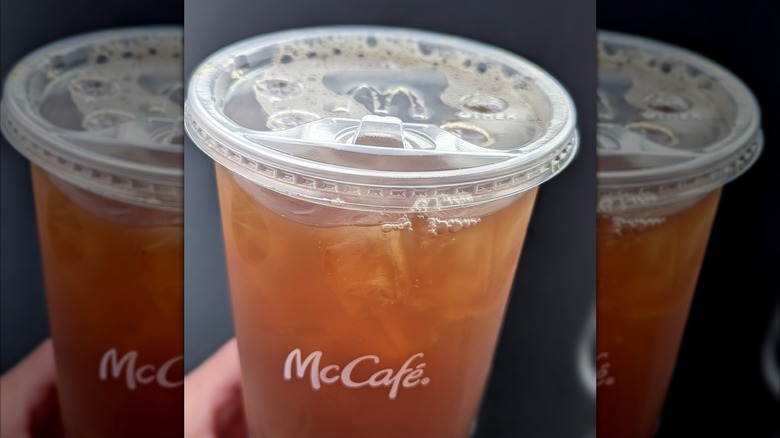 A person holding a McDonald's sweet tea in a plastic cup