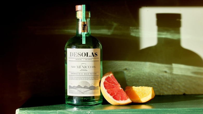 A bottle of Desolas mezcal next to grapefruit and orange slices