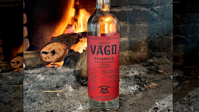 A bottle of Vago Tobala En Barro mezcal in front of a wood-burning oven