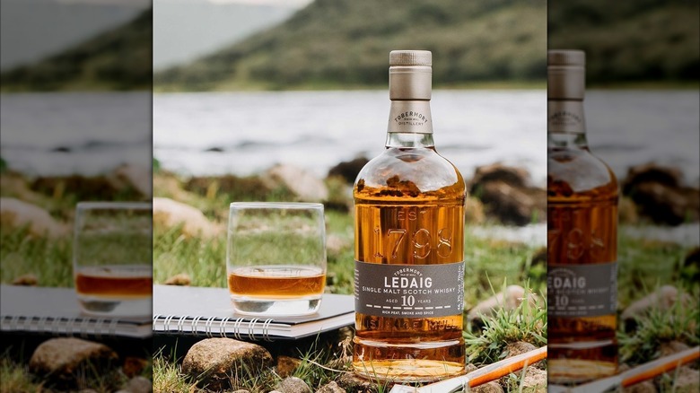 A bottle and glass of Ledaig 10 Year Single Malt Scotch Whisky on grass with water in the background