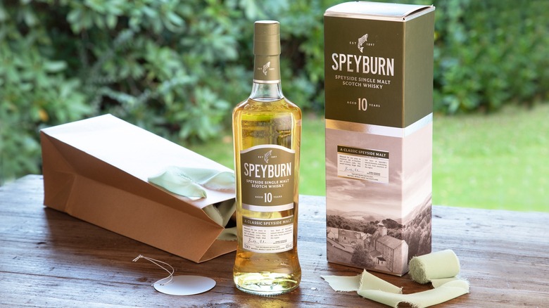 A bottle of Speyburn 10 Year Speyside Single Malt Scotch Whisky next to a gift bag and its box on a table outside