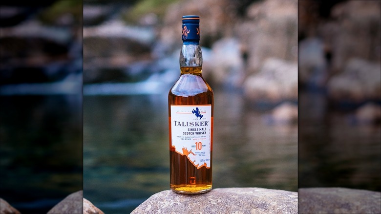 A bottle of Talisker 10 Year Single Malt Scotch Whisky on a rock next to water