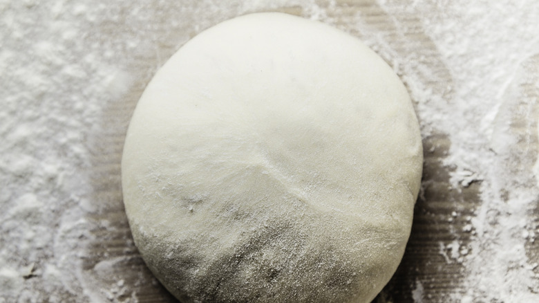 A ball of pizza dough is sitting on floured board