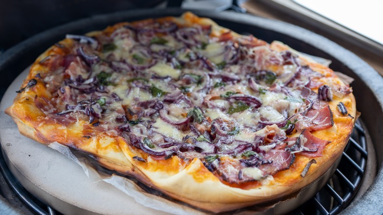 pizza is sitting on a pizza stone that is on top of a grill grate