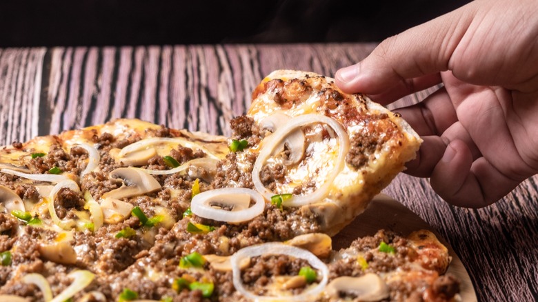 heavy, droopy, overloaded pizza with hand grabbing a slice