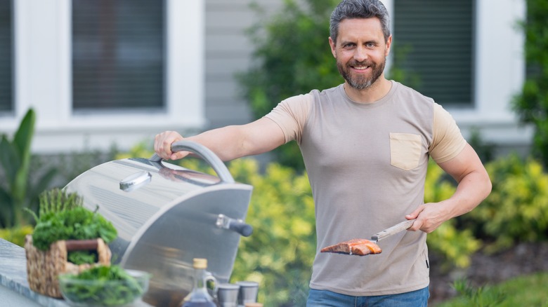 Man is standing outdoors next to a gas grill with the lid open