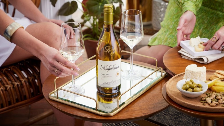 Bottle of wine on a tray surrounded by glasses, cheese, and olives