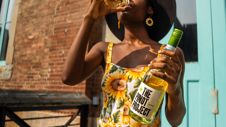 Woman holds a bottle of The Pinot Project wine and drinks a glass