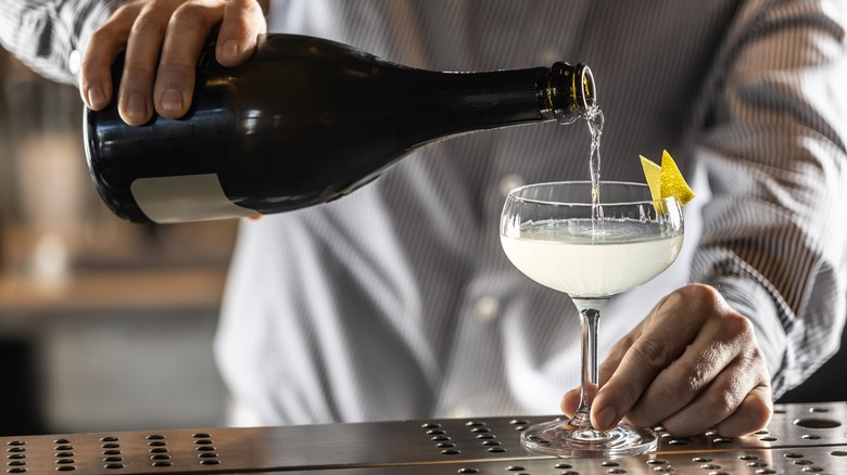 A bartender pouring champagne into a French 75 cocktail