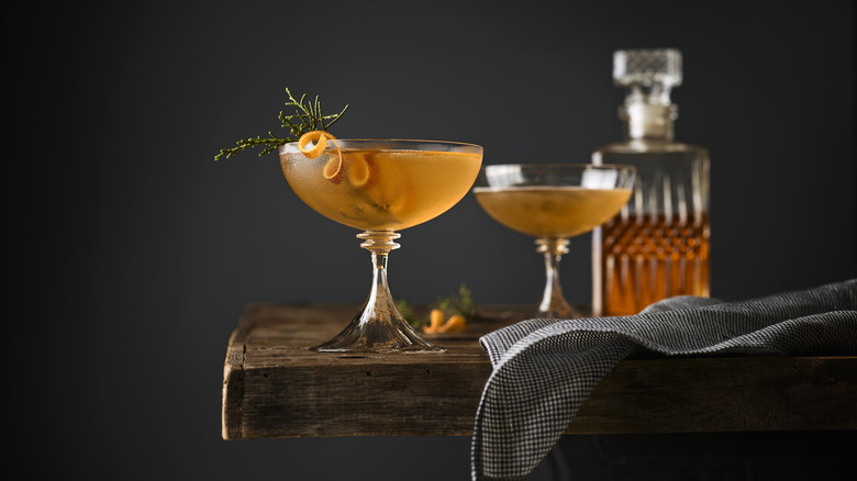 Two Manhattan cocktails on a table with a decanter of whisky