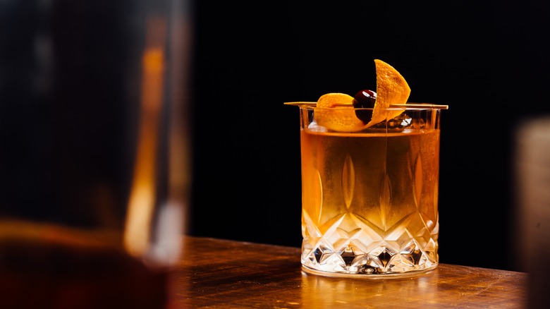 An Old Fashioned cocktail garnished with orange peel and a cherry