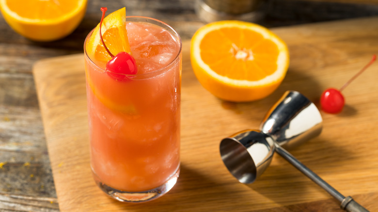A Sex on the Beach cocktail on a cutting board with oranges and cherries