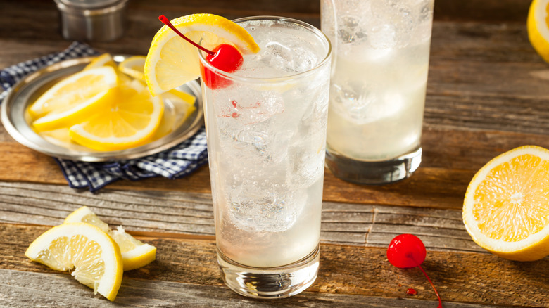 A Tom Collins cocktail garnished with a slice of lemon and a cherry