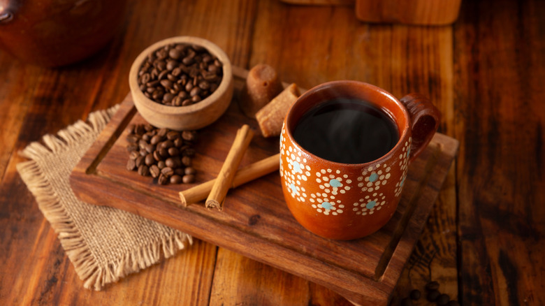 A serving tray with a cup of café de olla, cinnamon sticks, and coffee beans